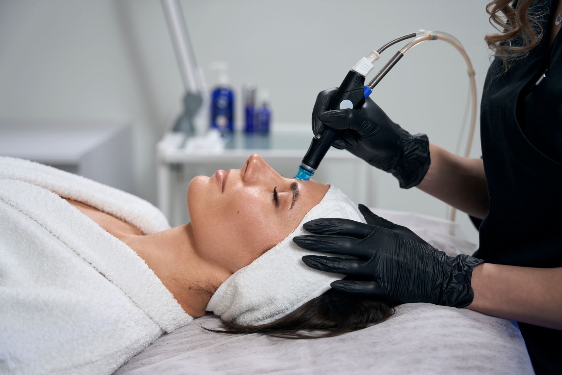 Kosmetikerin fuehrt eine Hydrafacial Behandlung im Gesicht durch