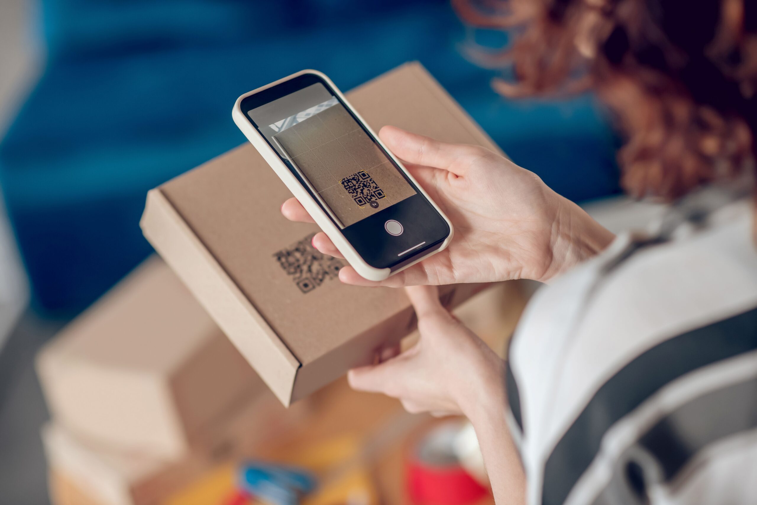 Person scannt mit dem Smartphone ein digitales Etikett mit QR-Code auf einem Versandkarton