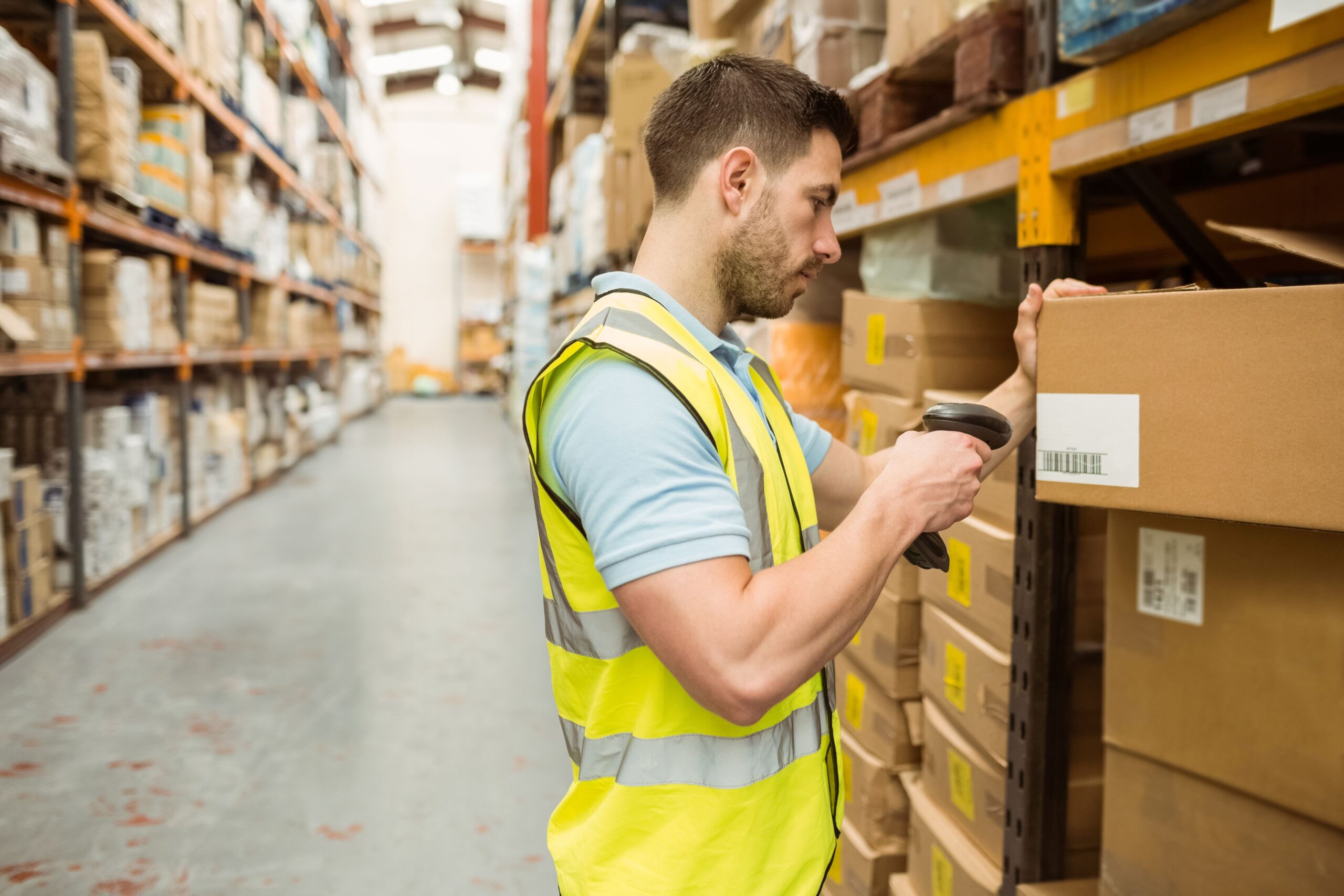 Lagerarbeiter scannt ein Etikett mit Barcode auf einem Kartonregal zur Prozesssteuerung in der Logistik